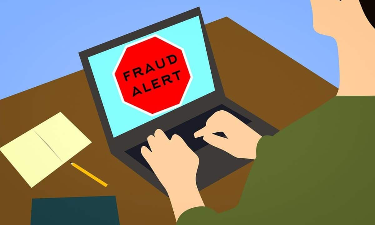 A cartoon of a person typing on a laptop computer. There is a fraud alert sign on the screen. The text in the sign says "FRAUD ALERT"