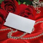 Romantic image of red roses, pearls, and a card on red satin.