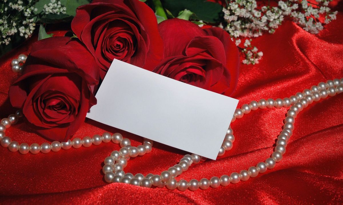 Romantic image of red roses, pearls, and a card on red satin.